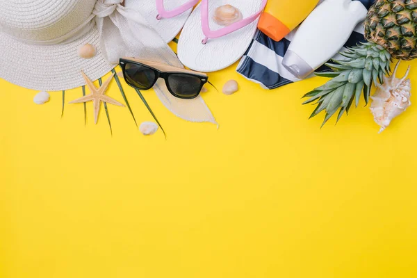 Плоские пляжные аксессуары: купальник, солнцезащитные очки, шляпа, сандалии с пальмовыми ветвями, экзотические фрукты и раковины. Вид сверху на желтый фон — стоковое фото