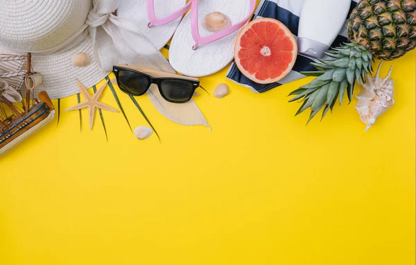 Flat lay beach accessories: swimsuit, sunglasses, hat, sandals with palm branches, exotic fruits and shells. Top view on yellow background — Stock Photo, Image