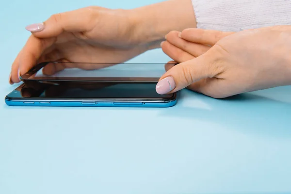 Smartphone con pantalla protege la cubierta de vidrio en las manos. fondo azul. mujer mano palo protector de vidrio templado o pantalla de película cubierta con teléfono móvil. conceptos protectores ideas — Foto de Stock