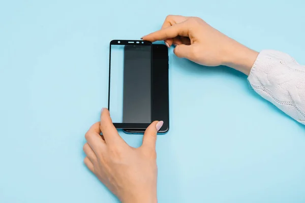 Smartphone con pantalla protege la cubierta de vidrio en las manos. fondo azul. mujer mano palo protector de vidrio templado o pantalla de película cubierta con teléfono móvil. conceptos protectores ideas — Foto de Stock