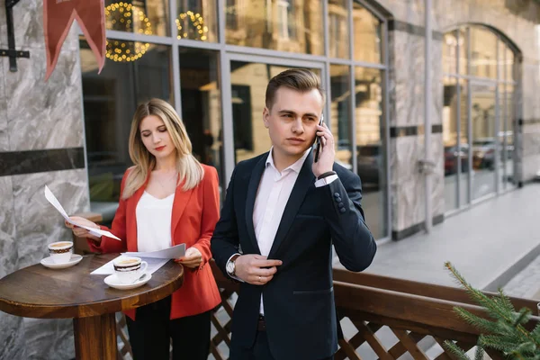 Business Woman and Business Man Use Smartphone y Talk on the Busy Big City Street (en inglés). Ambos se ven exquisitamente elegantes . — Foto de Stock