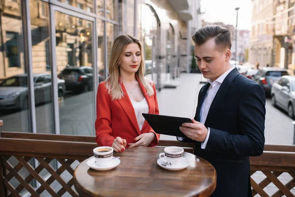 Executive colleagues remote working with tablet on coffee break outdoors. Successful businesspeople using digital device and holding coffee to go. Coffee break concept