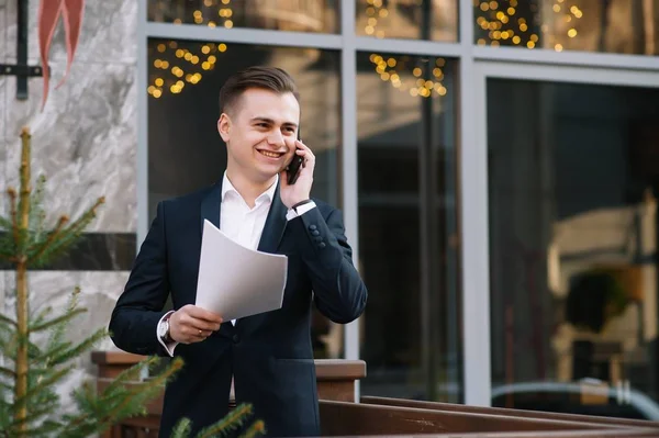 Jeune homme d'affaires avec documents et téléphone portable près du bâtiment moderne . — Photo