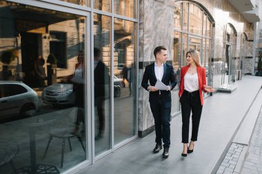 Ofis terasında yürüyen iki kendine güvenen iş arkadaşı. Orta yetişkin iş adamı ve kadın kahve molası açık havada belge tartışıyor. Mola konseptinde çalışma
