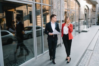 Ofis terasında yürüyen iki kendine güvenen iş arkadaşı. Orta yetişkin iş adamı ve kadın kahve molası açık havada belge tartışıyor. Mola konseptinde çalışma