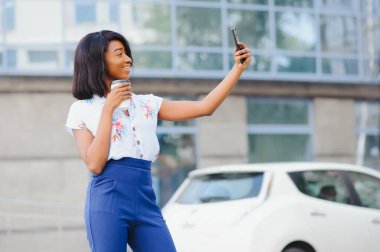 Güzel Afrikalı kadın cep telefonunun kamerasında poz veriyor, selfie çekiyor ya da video görüşmesi yapıyor.