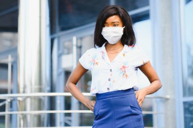 Şehirde yüzüne koruyucu maske takan Afro-Amerikalı bir iş kadını. Bir salgın sırasında iş ziyareti kavramı