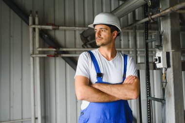 Young smiling professional in overalls and protective helmet standing in front of camera inside large machinebuilding plant