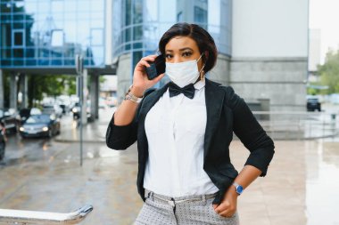 Şehirde yüzüne koruyucu maske takan Afro-Amerikalı bir iş kadını. Bir salgın sırasında iş ziyareti kavramı