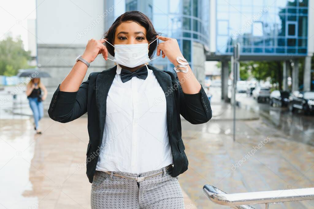 Beautiful african business woman in suit wearing surgical protect mask standing in a crowd of walking people. Concept for prevent for coronavirus outbreak