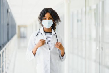 Kadın Amerikalı Afrikalı doktor, steteskop ve maskeli hemşire kadın. Arka planda poz veren başarılı bir tıp çalışanı olduğu için mutlu. Pandemia konsepti, covid 19