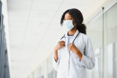Kadın Amerikalı Afrikalı doktor, steteskop ve maskeli hemşire kadın. Arka planda poz veren başarılı bir tıp çalışanı olduğu için mutlu. Pandemia konsepti, covid 19