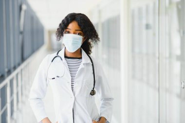 Kadın Amerikalı Afrikalı doktor, steteskop ve maskeli hemşire kadın. Arka planda poz veren başarılı bir tıp çalışanı olduğu için mutlu. Pandemia konsepti, covid 19