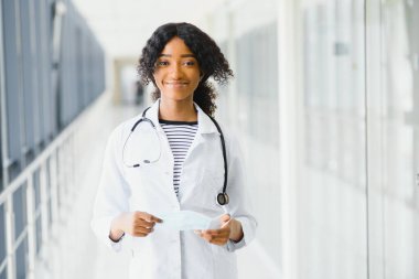 Kendine güvenen Afro-Amerikan kadın doktor profesyonel hasta notları hastane koridorlarının arka planında izole edilmiş. Pozitif yüz ifadesi