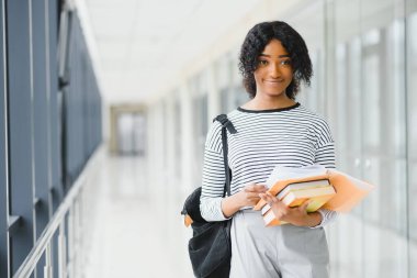 Parlak koridorda kıvırcık siyah saçlı Afrikalı bir üniversite öğrencisi portresi.