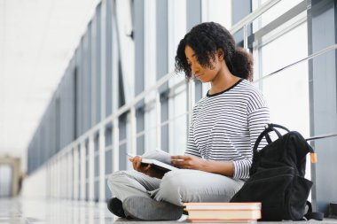 Parlak koridorda kıvırcık siyah saçlı Afrikalı bir üniversite öğrencisi portresi.