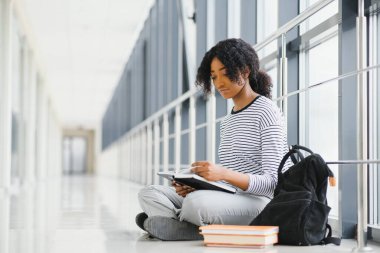 Afro-Amerikan öğrencinin yan görünüşü koridorda oturup kitap okuması.