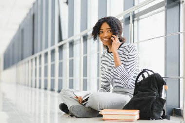 Parlak koridorda kıvırcık siyah saçlı Afrikalı bir üniversite öğrencisi portresi.