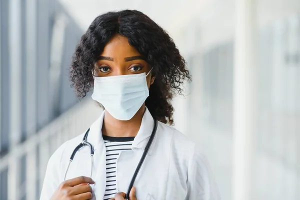 Kadın Amerikalı Afrikalı doktor, steteskop ve maskeli hemşire kadın. Arka planda poz veren başarılı bir tıp çalışanı olduğu için mutlu. Pandemia konsepti, covid 19