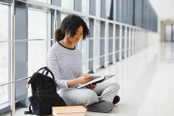 アフリカ系アメリカ人の学生が床に座り廊下で本を読んでいる姿を — ストック写真