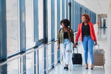 Gündelik giysiler içindeki genç Afrikalı Amerikalı bayan yolcu havaalanında telefonuyla bekliyor..