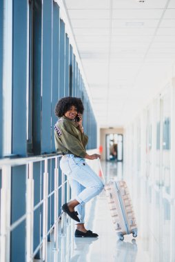 Bavul ve cep telefonuyla yürüyen mutlu bir kadın yolcunun tüm vücut profili.