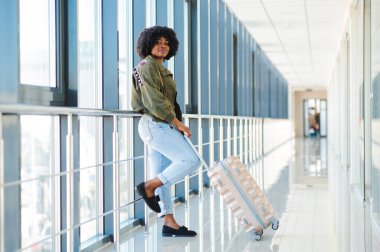 Gündelik giysiler içinde genç Afrikalı Amerikalı kadın yolcu havaalanında bagajlarıyla bekliyor..