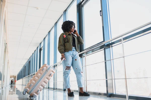 Full body profile portrait of happy female traveler walking with suitcase bag and cellphone