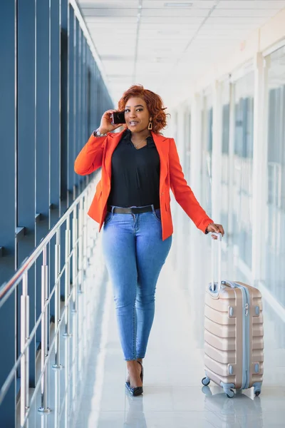 Full body profile portrait of happy female traveler walking with suitcase bag and cellphone