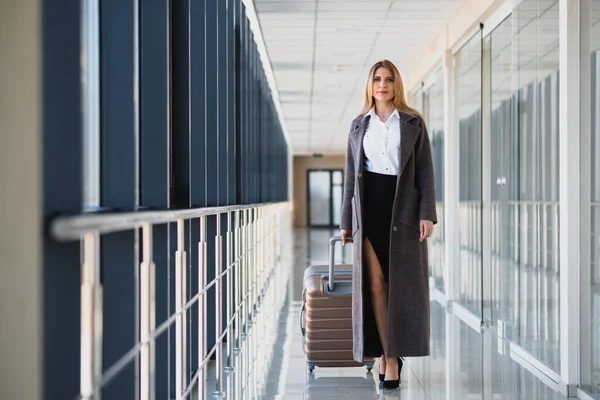 Portrait of successful business woman traveling with case at airport. Beautiful stylish female travel with luggage.