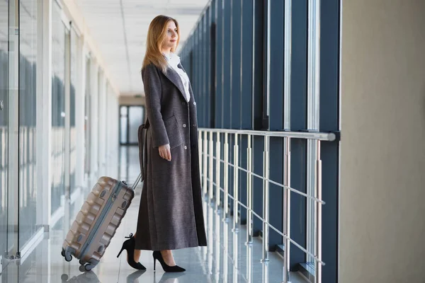 Portrait of successful business woman traveling with case at airport. Beautiful stylish female travel with luggage.