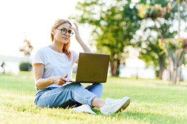 Çimlerin üzerinde dizüstü bilgisayarla çalışan güzel bir kadın. Uzaktan çalışma kavramı