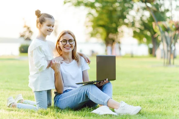 Funny mom and daughter with modern laptop outdoors