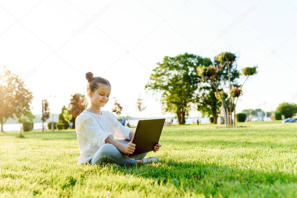 Little girl sitting in the park and working with laptop. Education, lifestyle, technology concept