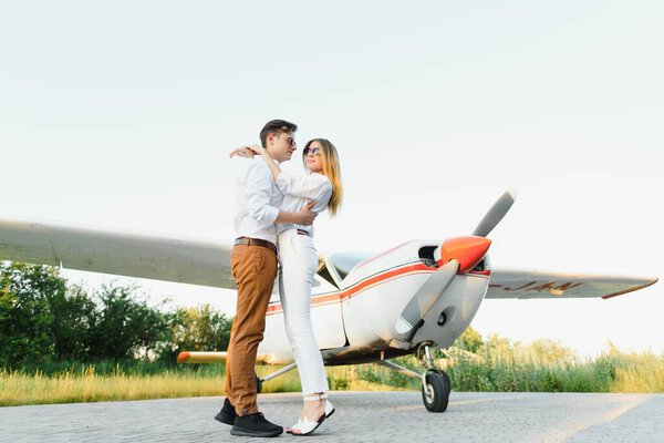 Full-length image of beautiful young stylish couple near private plane. Walking on runway in airport in front of airplane.