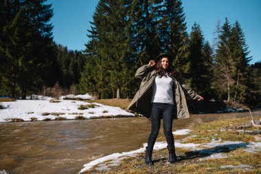 Ormanda gezen şık bir kız. Yaz ormanlarında gezen şapkalı genç bir kadın nehire bakıyor. Seyahat ve seyahat tutkusu konsepti. Metin için boşluk