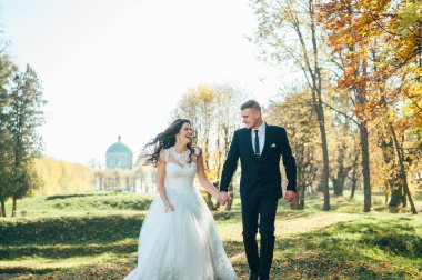 Mutlu gelin ve damadın güneş ışığı portresi gün batımında doğa alanında. Sıcak yaz zamanı. Güzel bir buket çiçekleri olan mutlu bir çift. Düğün fotoğrafı. Birbirine aşık bir çift. Sonbahar düğünü.