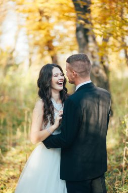 Damat yeşil parkta gülen gelinine sarılıyor. Düğün..