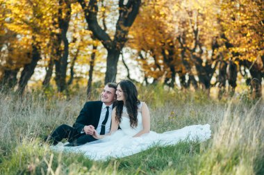 Mutlu gelin ve damadın güneş ışığı portresi gün batımında doğa alanında. Sıcak yaz zamanı. Güzel bir buket çiçekleri olan mutlu bir çift. Düğün fotoğrafı. Birbirine aşık bir çift. Sonbahar düğünü.