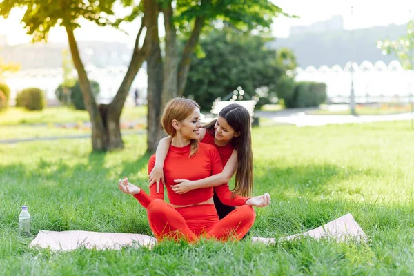 スポーツウェアを着た若い母親と娘が公園で一緒にヨガをします 家族の休日の概念 スポーツ フィットネス — ストック写真