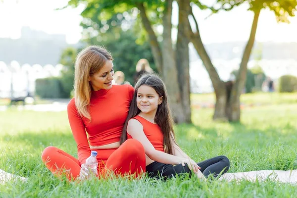 一位穿着运动服的年轻母亲和女儿一起在公园里做瑜伽 家庭假日的概念 — 图库照片