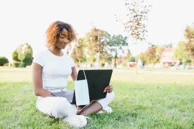 Zeki siyah kız, yaz parkında dizüstü bilgisayarıyla online çalışmalarına konsantre olmuş.