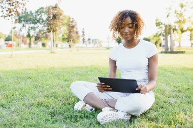 Çevrimiçi iletişim, eğitim veya iş kavramı. Parkta tablet bilgisayarı olan güzel Afrikalı Amerikalı bayan.