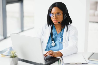 Genç Afro-Amerikalı doktor klinikte dizüstü bilgisayarla çalışıyor.