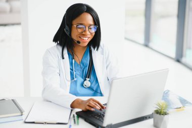 Afro-Amerikan mutlu gülümseyen genç doktor portresi. Kulaklık takan hasta telefonda. Çevrimiçi sağlık merkezi kavramı