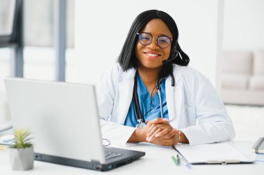 Afro-Amerikan mutlu gülümseyen genç doktor portresi. Kulaklık takan hasta telefonda. Çevrimiçi sağlık merkezi kavramı