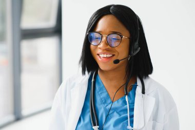 Afrikalı doktor kulaklık takıyor. Siyahi kadın hastaya danışıyor. Bilgisayarda web kamerasından görüntülü arama yapıyor. Teletıp video konferansı uzaktan bilgisayar uygulaması sanal toplantısı. Omuz üzerinden video çağrısı görünümü.