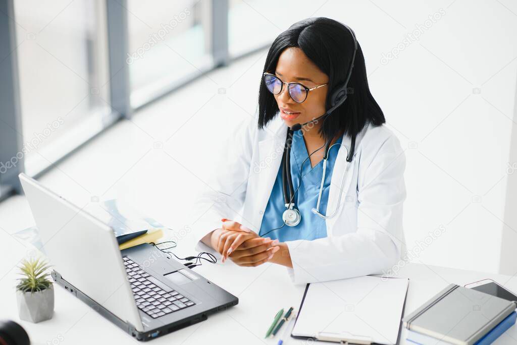 African doctor wear headset consult patient make online webcam video call on laptop screen. Telemedicine videoconference remote computer app virtual meeting. Over shoulder videocall view.