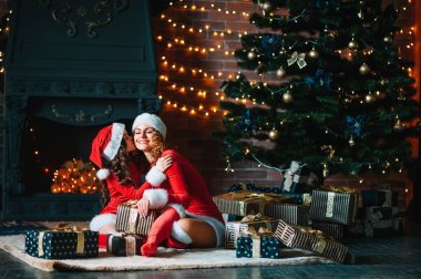 Mutlu Noeller ve mutlu tatiller! Noel kostümlü küçük kızı olan güzel bir anne Noel ağacının yanında birlikte vakit geçirir..