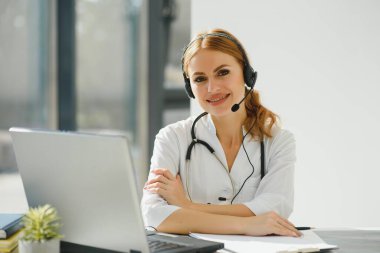 Genç bayan doktor, tıbbi ofisten hastayla konuşuyor. Hastanede görüntülü sohbet laptopunda hekim danışmanı